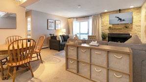 A living room with a fireplace, a television mounted on the wall, a dining area with wooden chairs and a table, and a sofa set. - Beautifully, Cozy Condo, Steps from Complimentary Shuttle, Free parking (Vail)