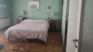 A bedroom with a bed, two bedside tables with lamps, a wooden floor, a door, and a framed picture on the wall. - B&B Bam Bam (Bergamo)