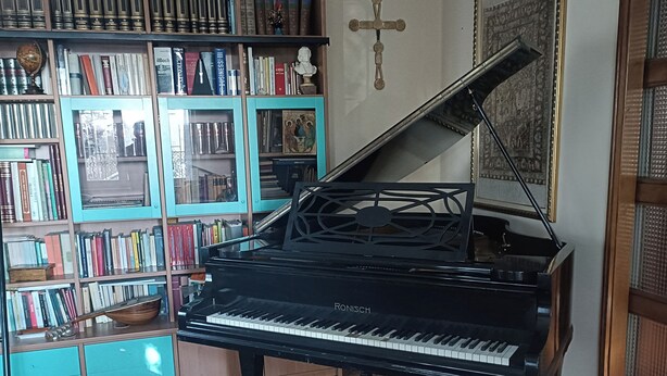 A grand piano in a room with wooden floors and a bookshelf filled with books and decorative items. - B&B Bam Bam (Bergamo)