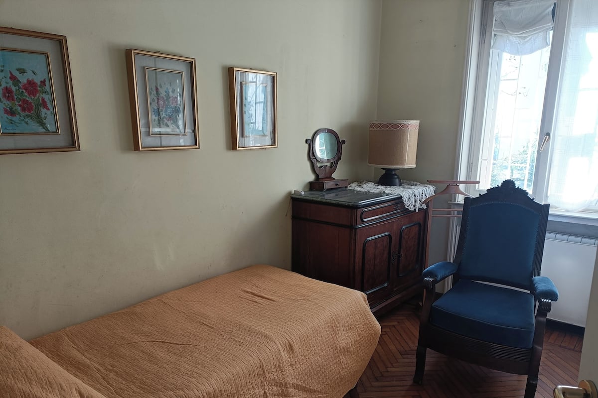 A room with a bed, a chair, a wooden cabinet, and three framed pictures on the wall.