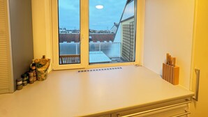 A kitchen with a large window, a white countertop, and a view of neighboring buildings.