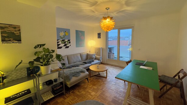 A cozy living room with a sofa, a dining table, and a large window.