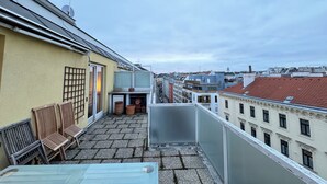 A rooftop terrace with a table, chairs, and potted plants.