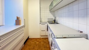 A modern kitchen with white cabinets, a wooden herringbone floor, a built-in dishwasher, and a stainless steel sink.