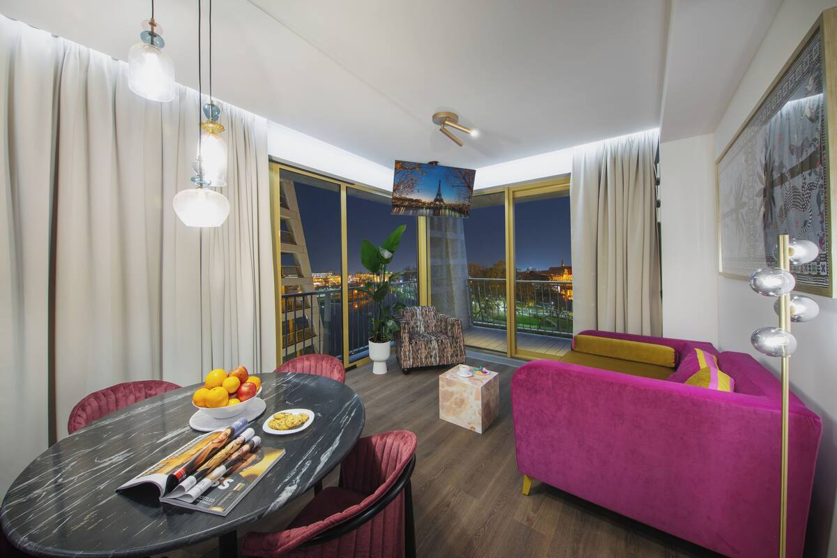 Un salon moderne comprenant un coin repas, un canapé rose vif et un balcon offrant une vue sur la ville.