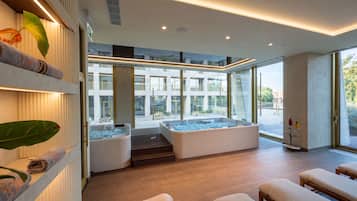 A modern spa area with two hot tubs, a wooden floor, and a view of a building with balconies.