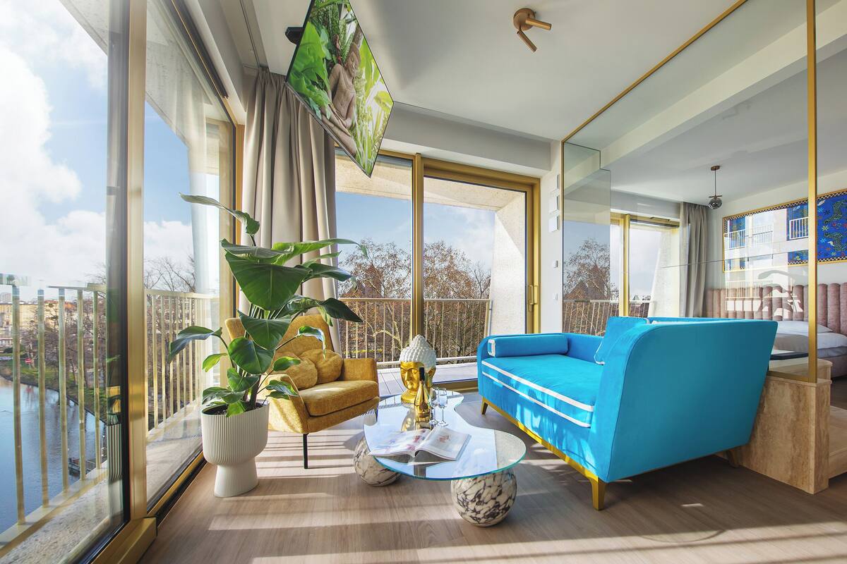 Un salon moderne avec un canapé bleu, une statue de Bouddha dorée et une grande fenêtre donnant sur un balcon.