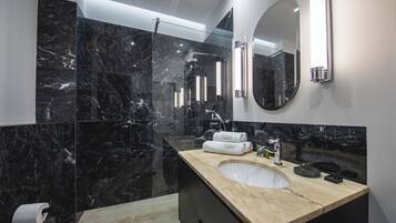 A modern bathroom with a marble sink, a large mirror, and a glass-enclosed shower.