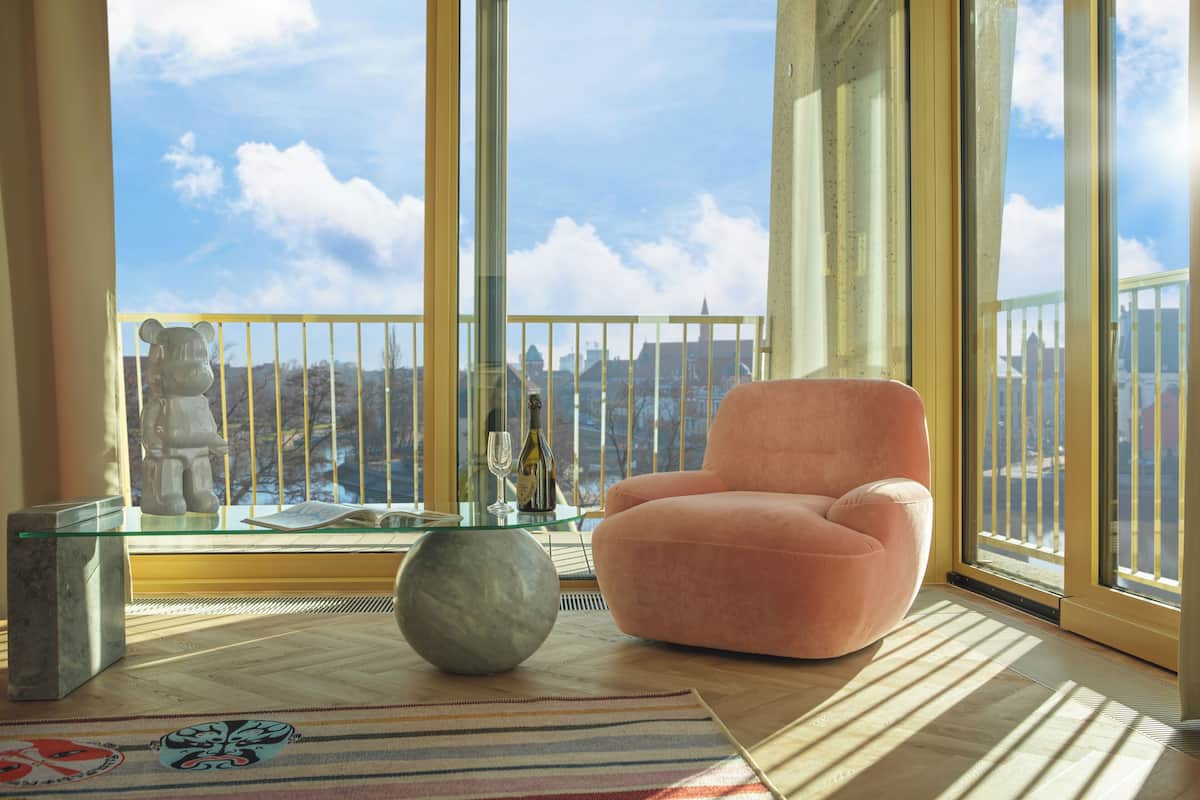 Un salon moderne avec un fauteuil rose, une table basse en verre et une statue d’ours décorative.