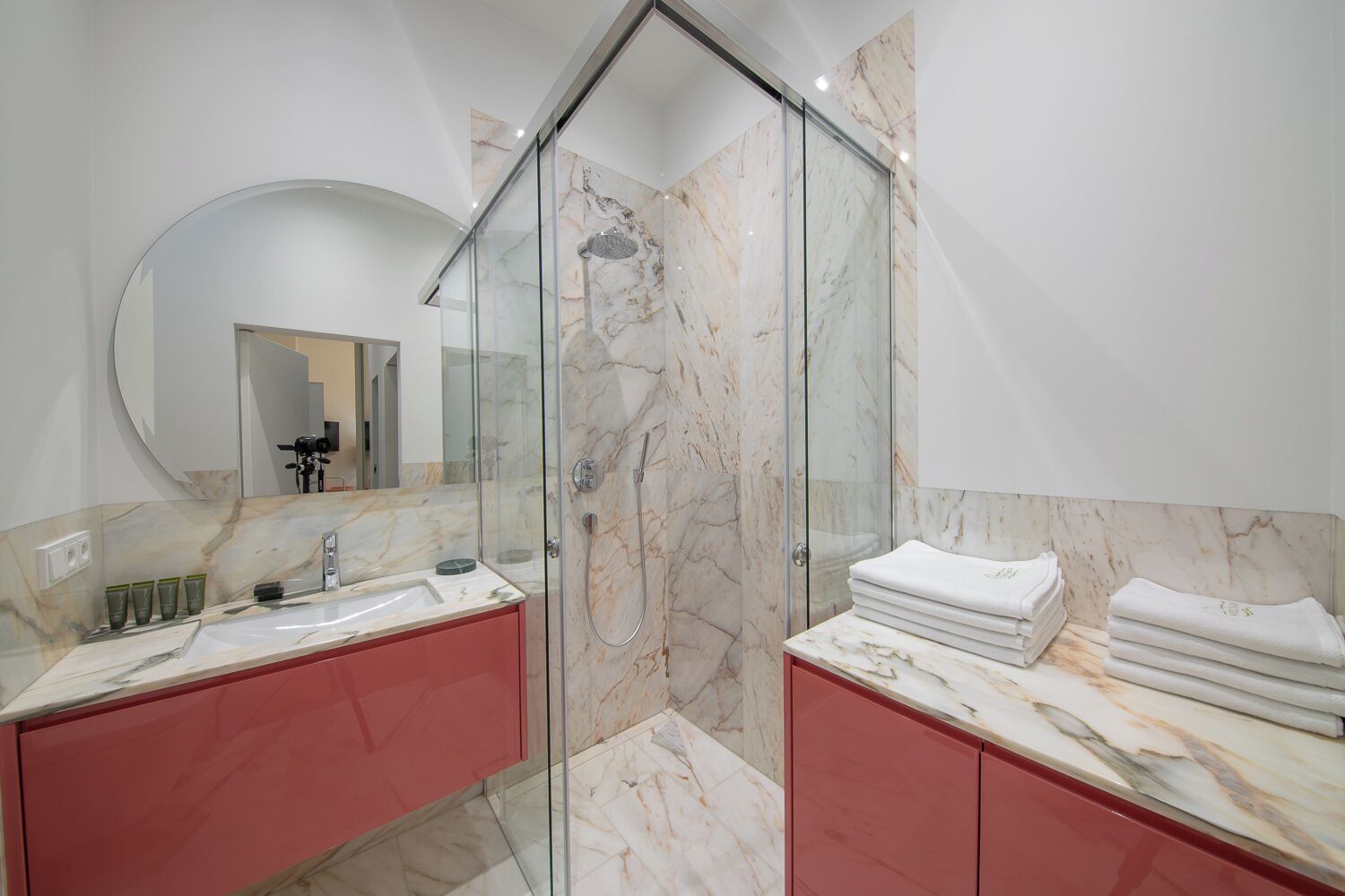 Un baño moderno con ducha de vidrio, dos lavamanos con encimeras de mármol y un espejo grande.
