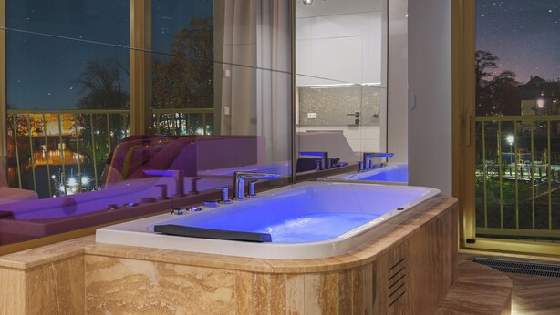 A modern spa area with a hot tub, seating, and a large window offering a night view. - Boulevard Drobnera Residence (Wroclaw)