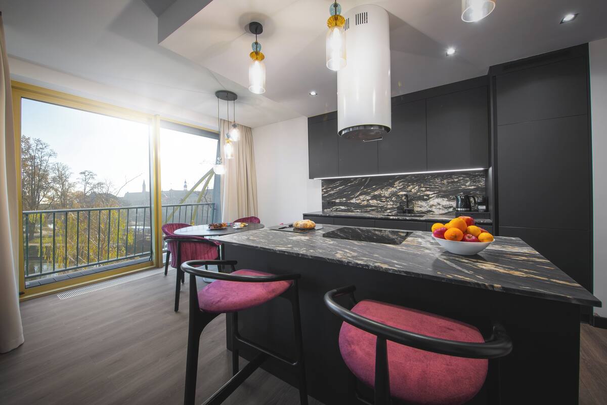 Une cuisine moderne dotée d’un îlot en marbre, de luminaires suspendus et offrant une vue sur l’extérieur.