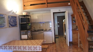 Een kleine keuken met een eettafel en bankjes, een houten trap en een betegelde vloer.