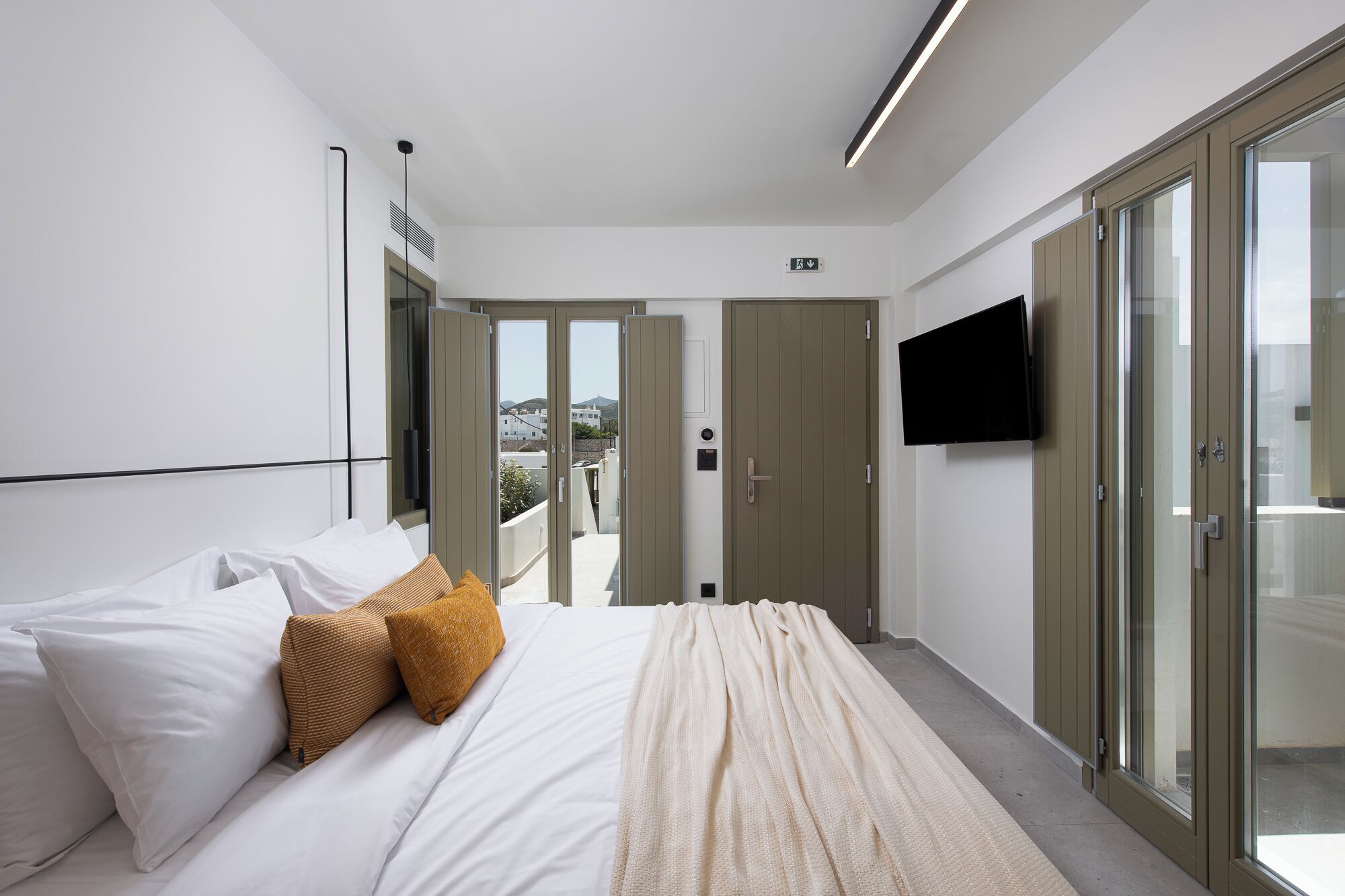 Un dormitorio moderno con una cama grande, un televisor montado en la pared y un ventanal corredero que da a un espacio exterior.