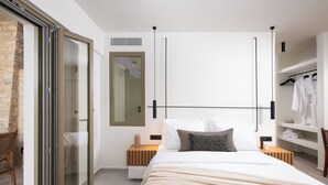 A modern bedroom with a bed, a wardrobe, a mirror, and a seating area with a chair. - Mazee Paros (Paros)