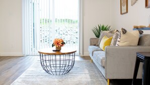 Ein Wohnzimmer mit einer Couch, einem Couchtisch und einem großen Fenster mit Jalousien.