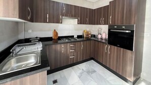 Une cuisine moderne avec des meubles de couleur bois foncé, un plan de travail noir, des appareils en acier inoxydable et un pare-feu en carreaux.