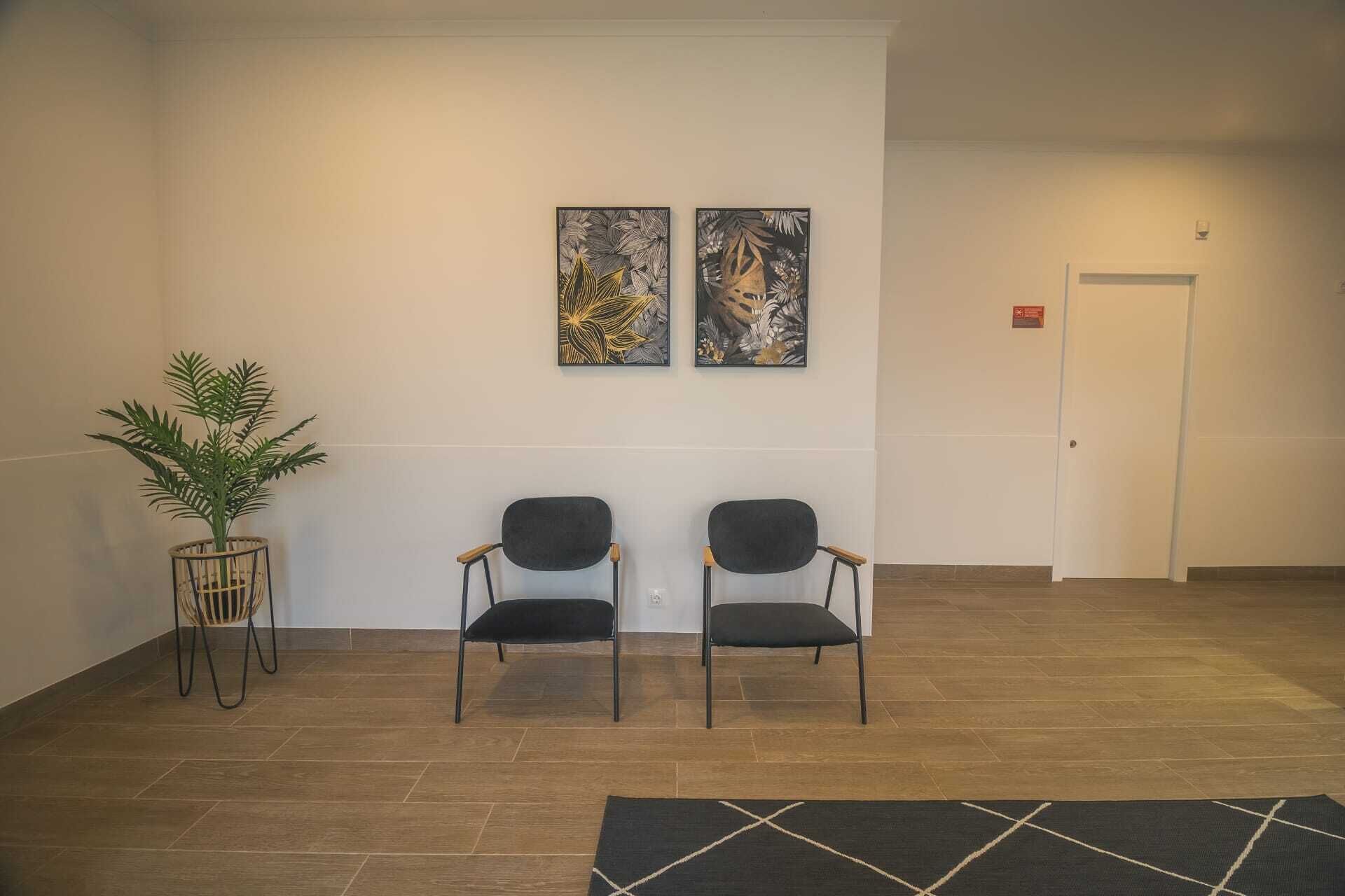 A reception area with two chairs, a potted plant, and two framed artworks on the wall.