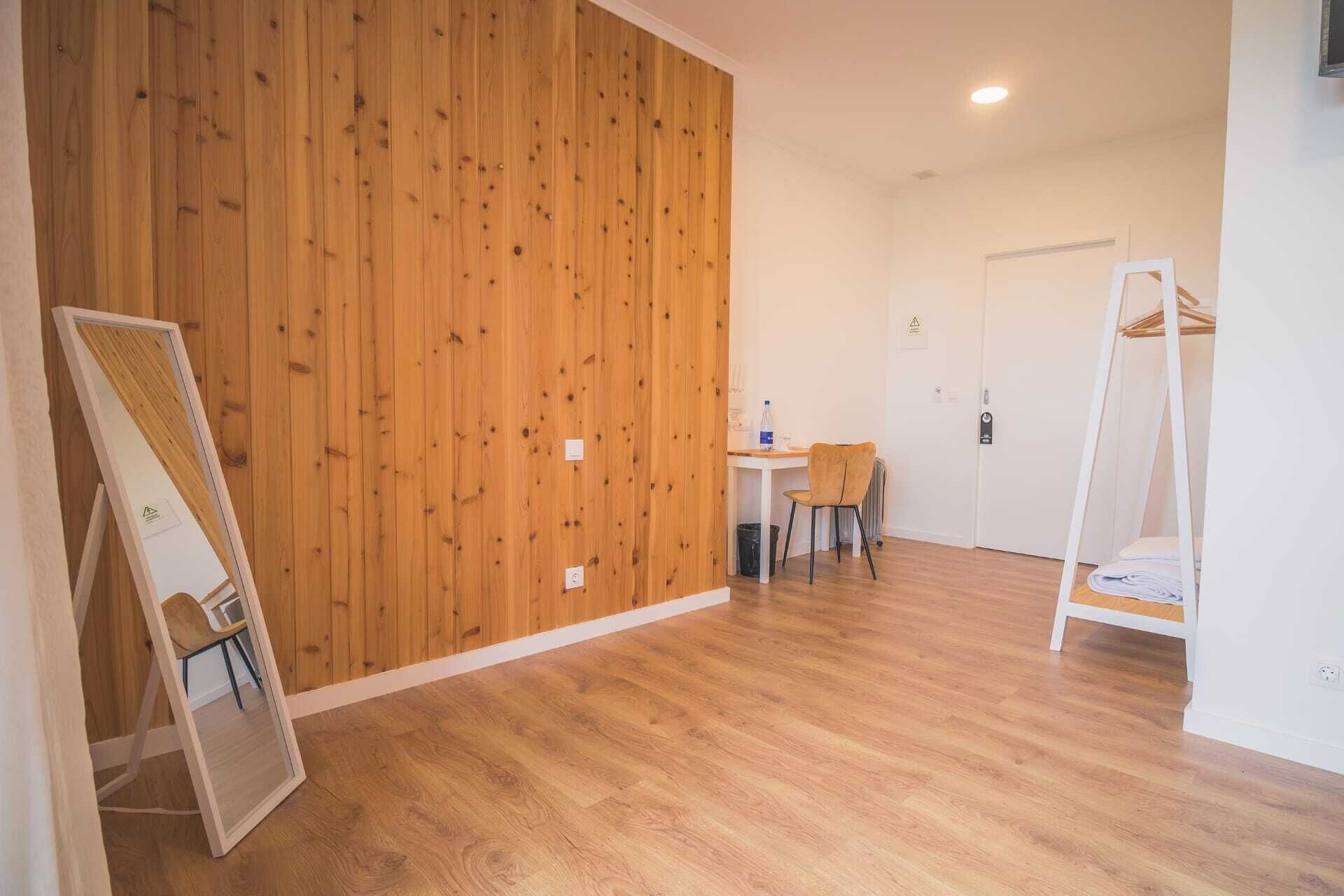 A room with a wooden panel wall, a white door, a small table with a chair, and a white shelf unit.