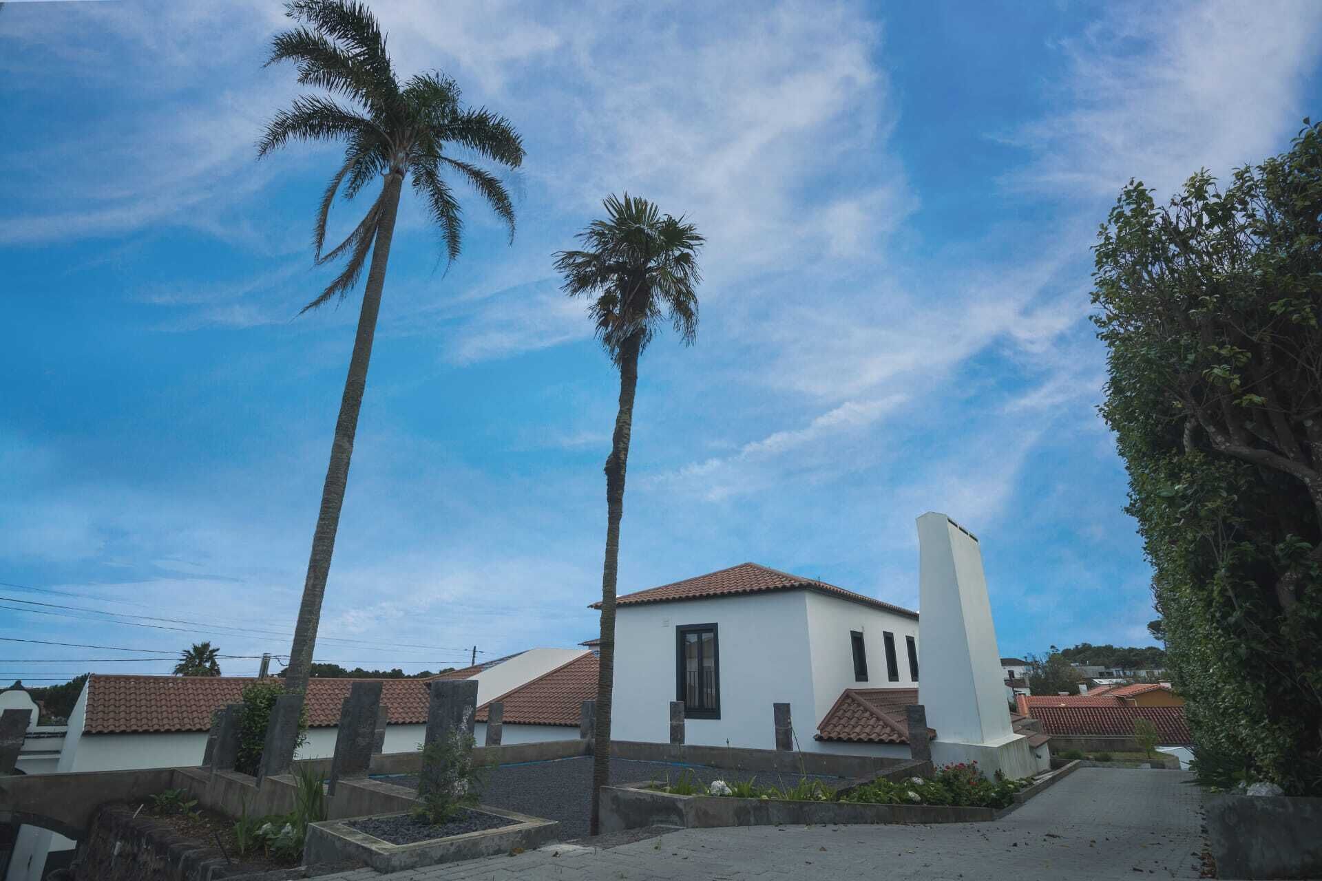 A white building with a red-tiled roof, surrounded by palm trees and a clear sky.