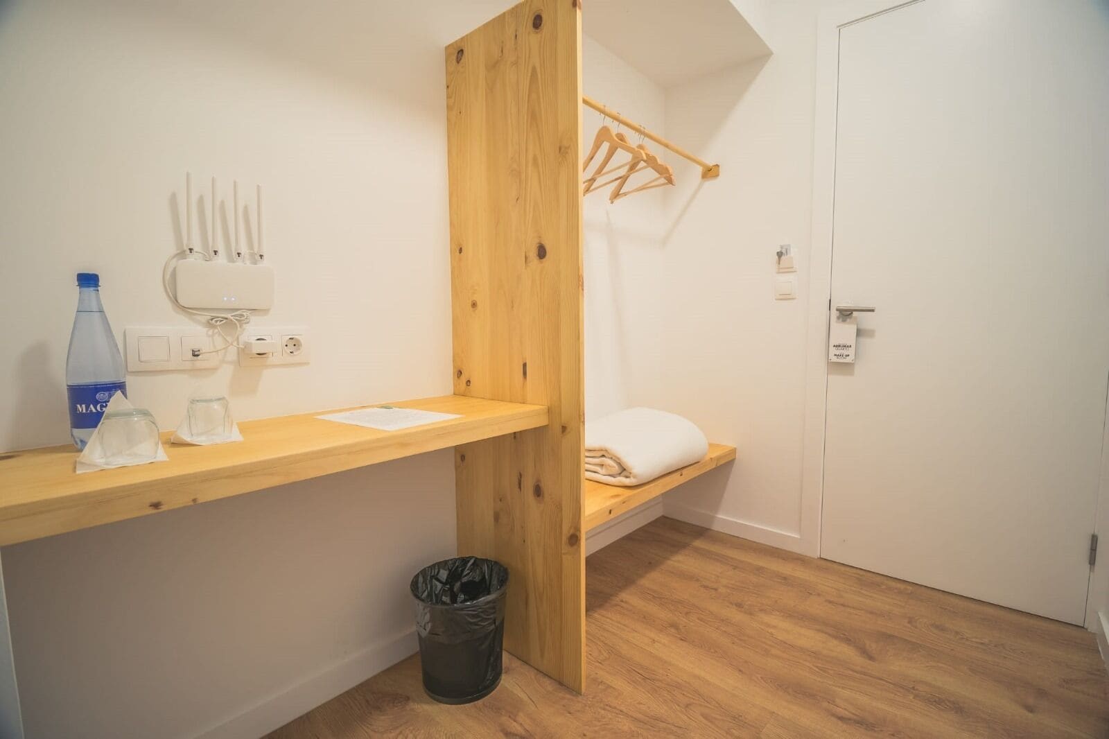 Een kleine, compacte kamer met een houten stapelbed, een houten bureau met een waterfles, glazen en een prullenbak.