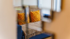 Un salon avec un canapé bleu, deux coussins jaunes et un plaid à motifs.