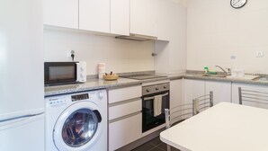 Une cuisine compacte équipée d’un four à micro-ondes, d’un four et d’un lave-linge, avec une horloge au mur et un petit coin repas.
