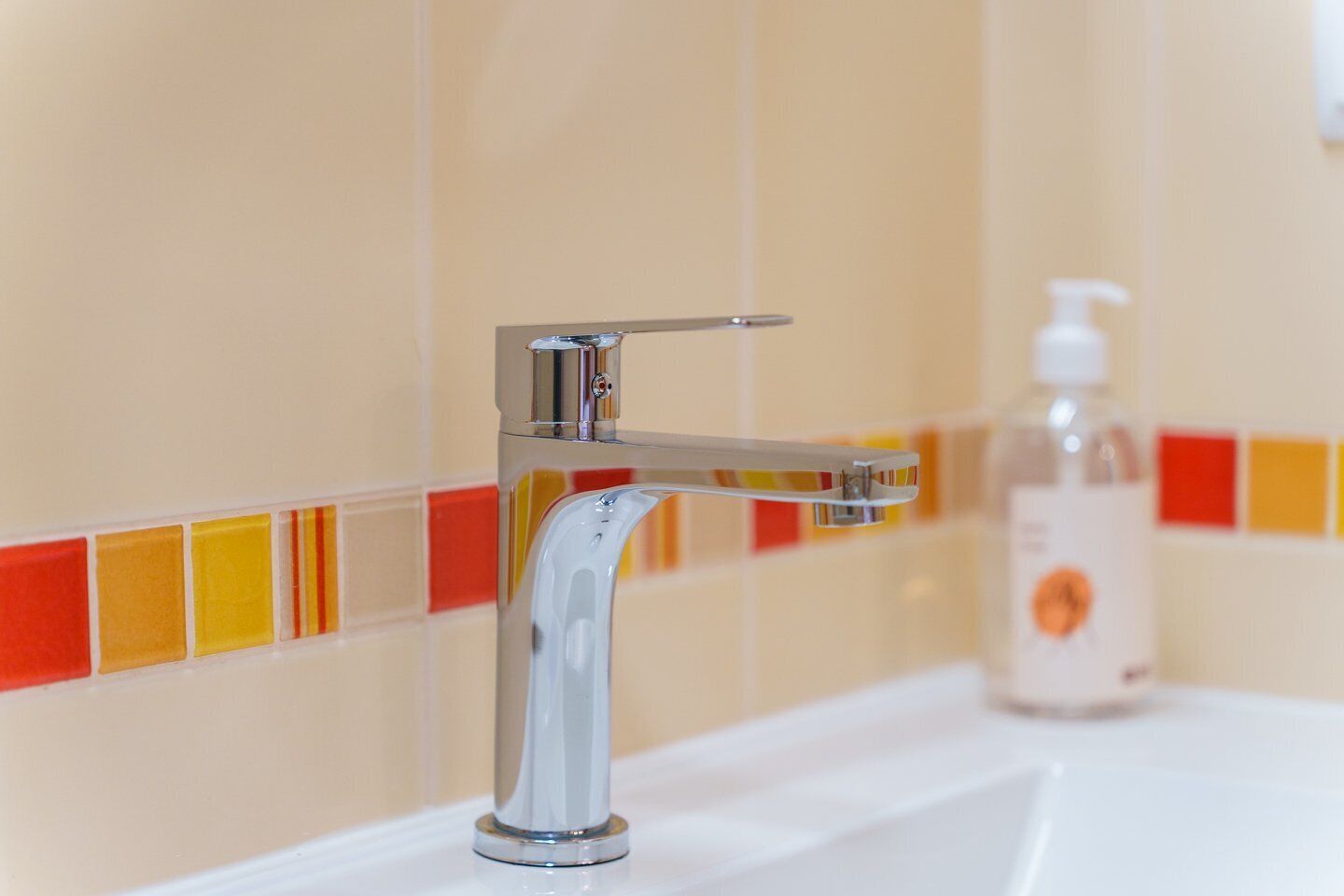 Un baño con grifo cromado y dispensador de jabón en el lavabo.