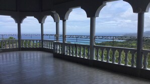 A covered balcony with a view of the sea and greenery.