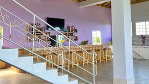 A spacious interior with a high ceiling, a staircase with metal railings, and a bar area with stools and shelves of bottles.