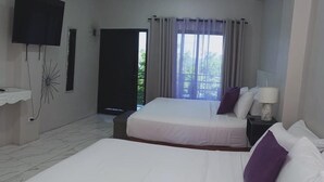 A hotel room with two beds, a TV, a window with curtains, and a view of greenery outside.