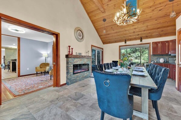 Un espace repas doté d’un plafond en bois, d’une cheminée et offrant une vue sur l’extérieur.