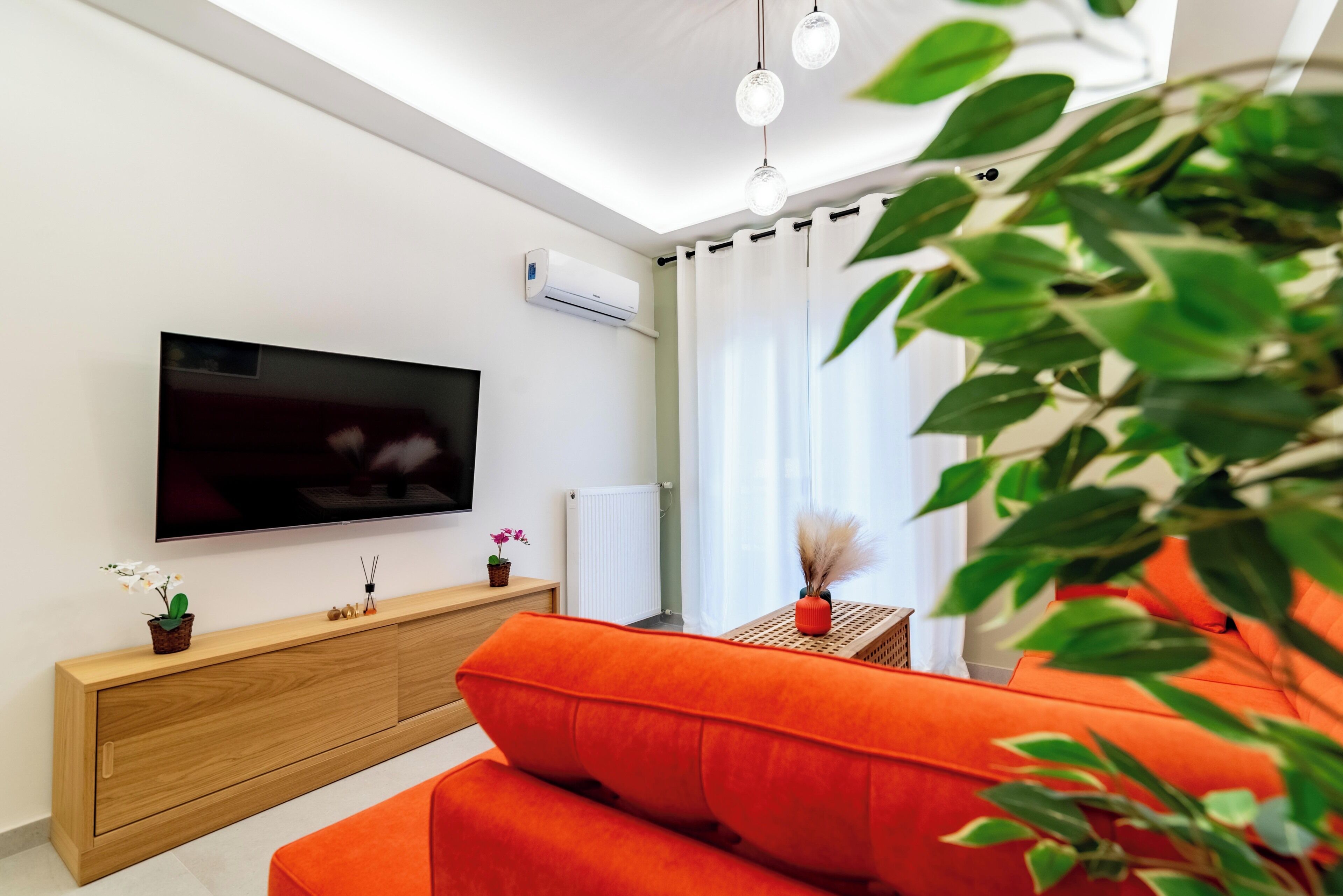 Ett modernt vardagsrum med en platt-TV, en träkonsol, en orange soffa och ett litet bord med dekorativa föremål.