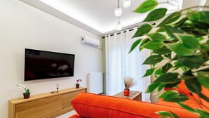 Un salon moderne doté d’un téléviseur à écran plat, d’une console en bois, d’un canapé orange et d’une petite table agrémentée d’objets décoratifs.