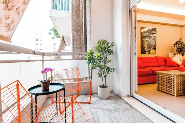 A balcony with a table and chairs, a potted plant, and a red sofa inside a room. - Psirri Urban Chic · Central 3BR · Sleeps 10 (Athina)