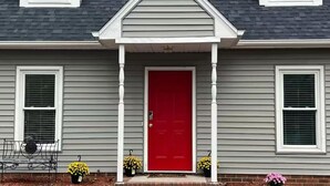 A house with a red door, grey siding, and a small porch with two potted plants. - Spacious Charming 3-bedroom house with WiFi and AC in Burlington (Burlington)