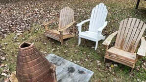 Three Adirondack chairs and a rustic wooden planter on a grassy area with scattered leaves. - Spacious Charming 3-bedroom house with WiFi and AC in Burlington (Burlington)