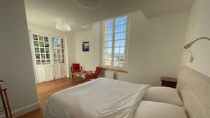 Une chambre avec un grand lit, une chaise, une table et une fenêtre.