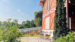 Un bâtiment traditionnel à colombages, doté d’une clôture en piquets blancs et d’un espace extérieur aménagé pour s’asseoir.