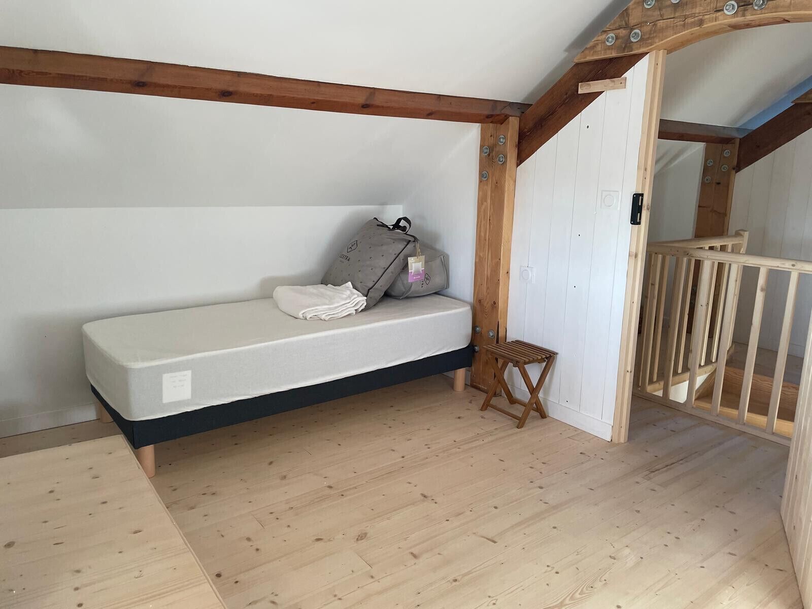 Ein kleiner, gemütlicher Raum mit einem Einzelbett, einem Holzschemel und einer Holztreppe.
