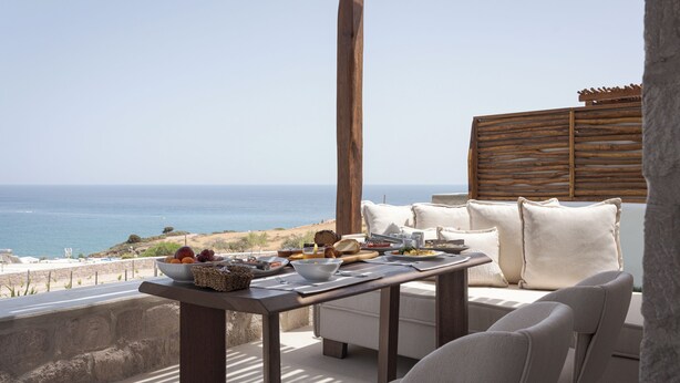 Une terrasse avec une table dressée pour le petit-déjeuner, offrant une vue sur la mer et le littoral.