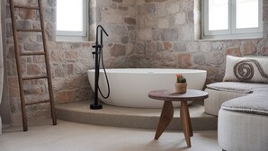 Une salle de bain aux murs de pierre, avec une baignoire, une échelle en bois et une petite table sur laquelle est posée une plante en pot.
