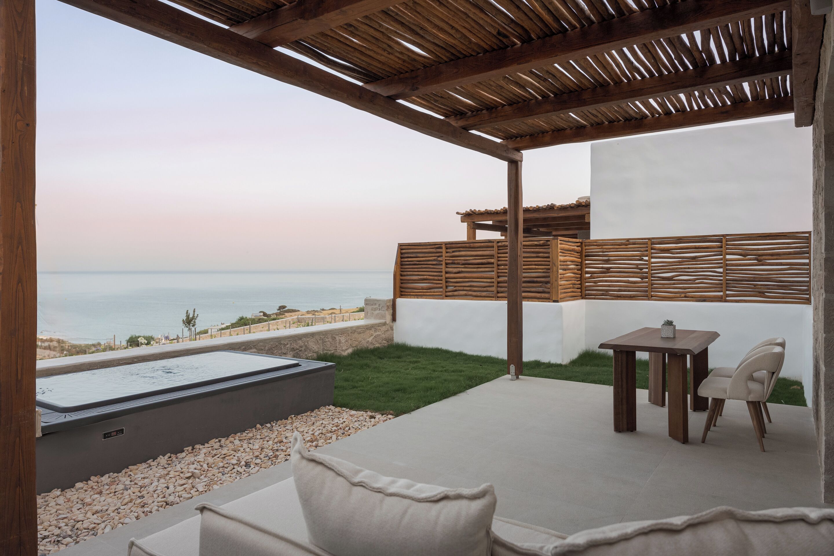 A covered outdoor area with a hot tub, a table, and chairs, overlooking a body of water.