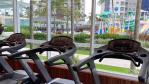 A gym with treadmills, large windows, and a view of outdoor palm trees and buildings. - Salinas Exclusive Resort (Salinópolis)