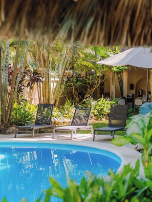A pool area with lounge chairs and a white umbrella, surrounded by tropical plants and bamboo. - Casa Real Sayulita Hotel Boutique (Sayulita)