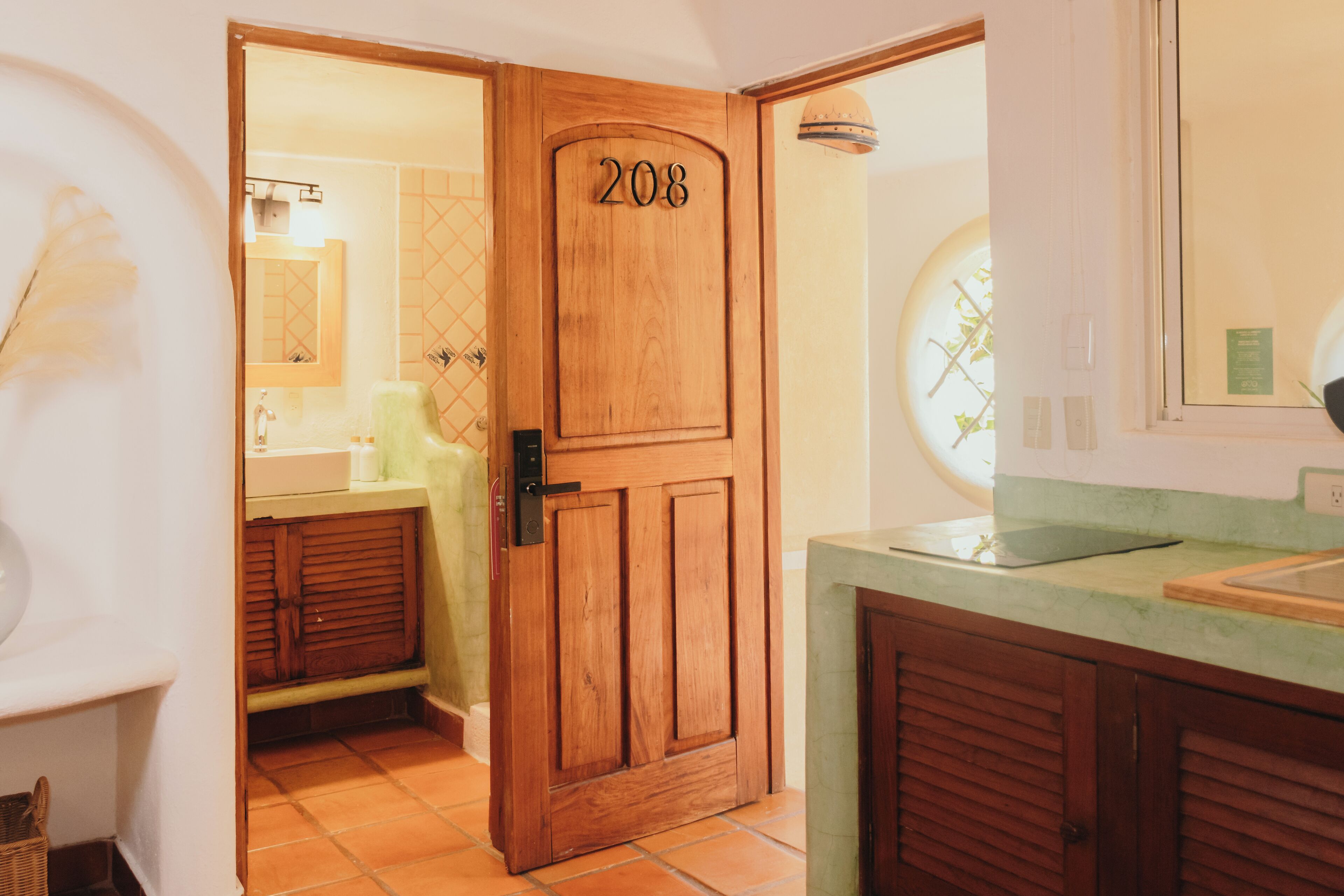 Una puerta de madera con el número 208, que da a un baño con un lavamanos verde y un espejo.