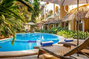 A pool area with lounge chairs, a thatched roof structure, and lush greenery. - Casa Real Sayulita Hotel Boutique (Sayulita)