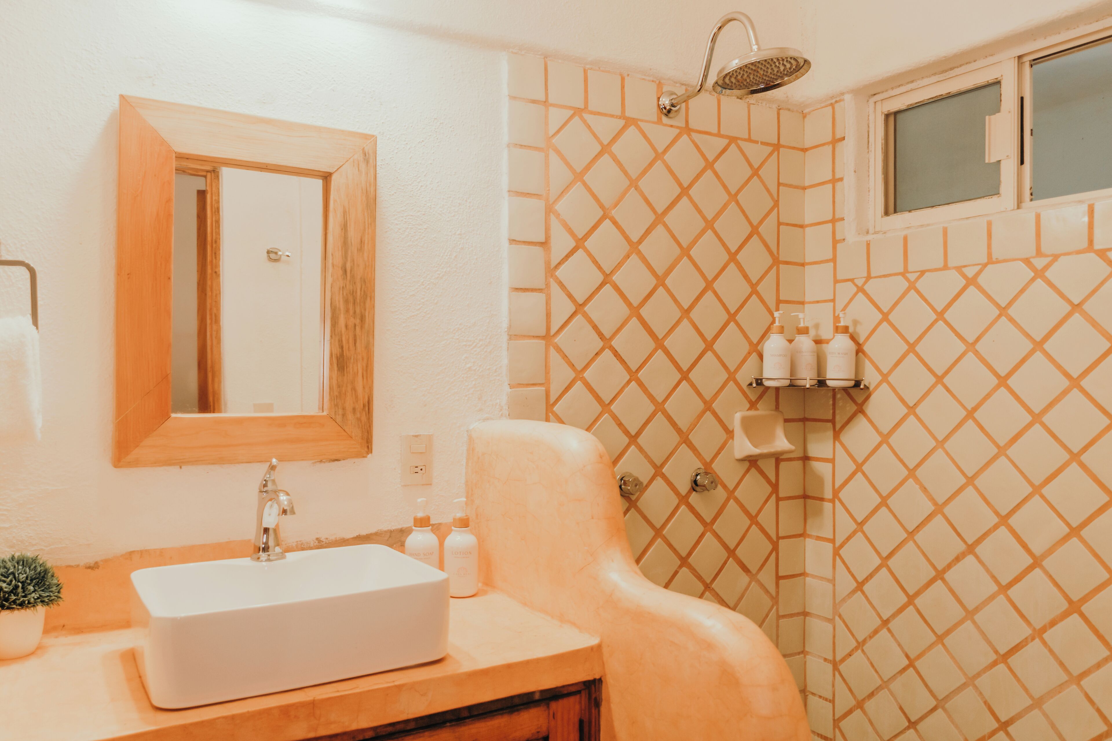Een badkamer met een wit wastafel, spiegel, douche en betegelde wanden.
