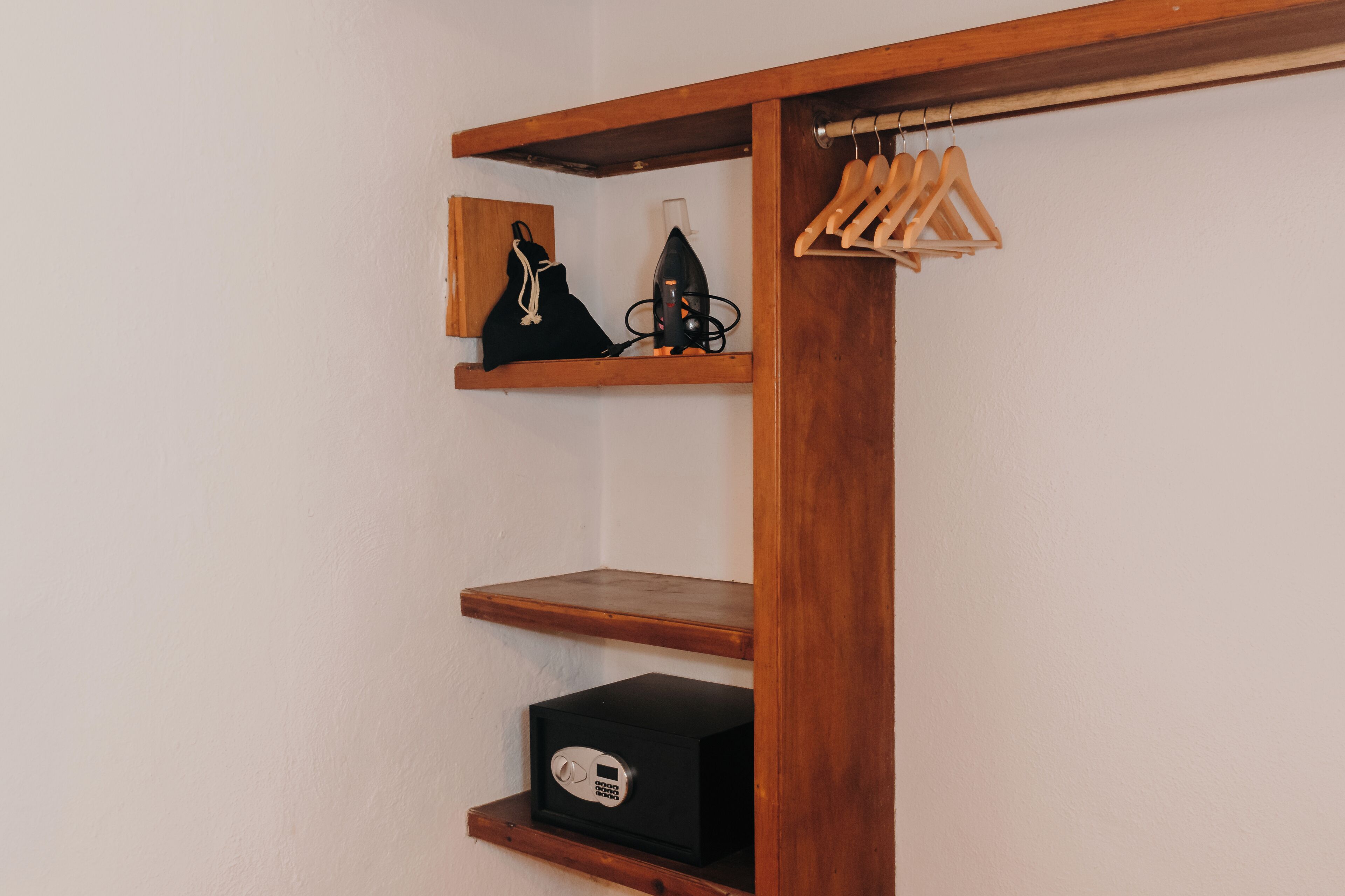 Un armario de madera con estantes, una barra para colgar ropa y una pequeña caja fuerte.