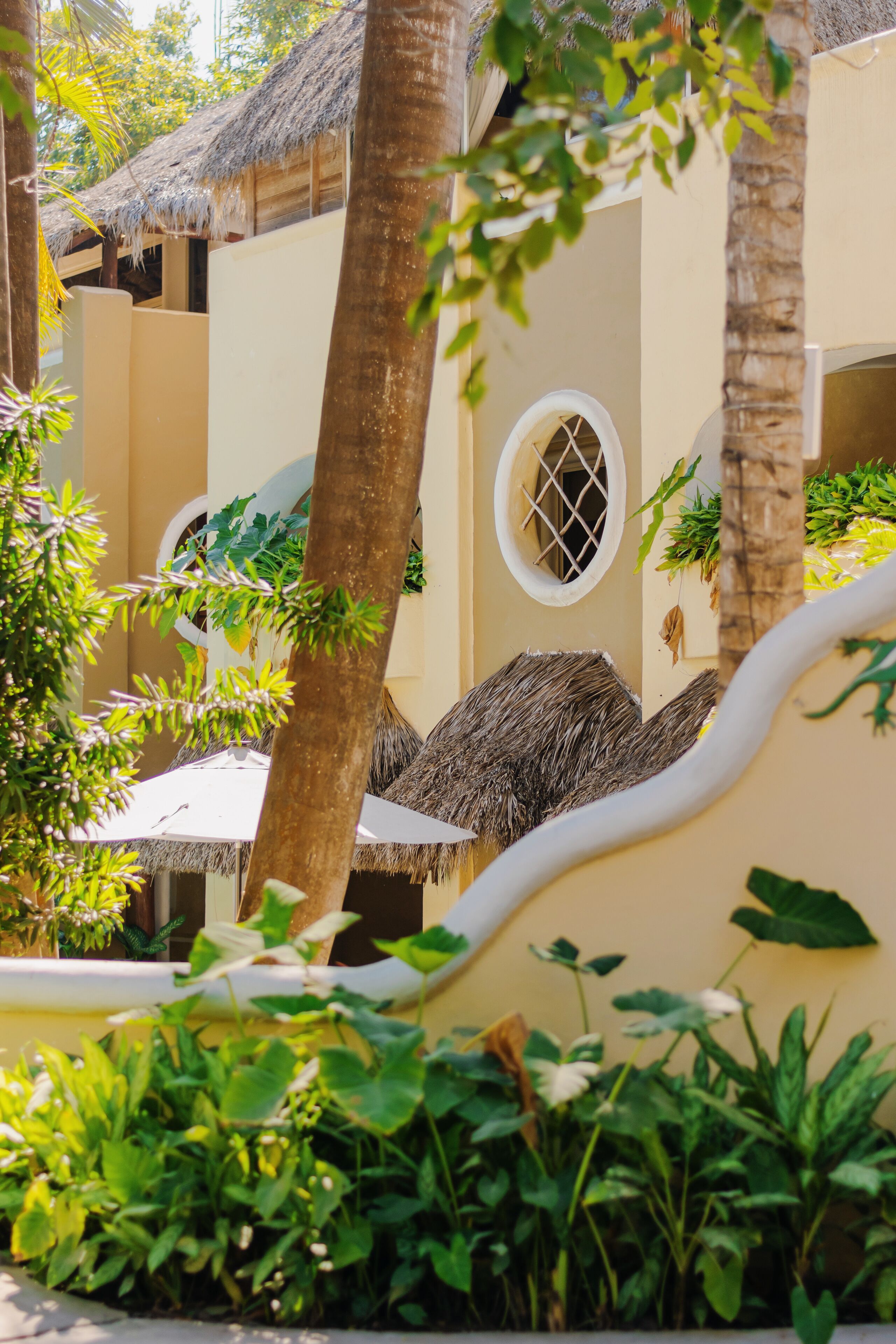Un resort con estructuras de techo de paja, palmeras y exuberante vegetación.